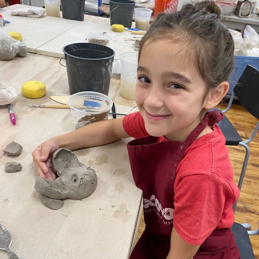 Child posing proudly with their sculpture of a smiling animal