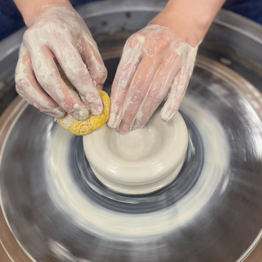 Throwing clay on a wheel with a sponge in one hand