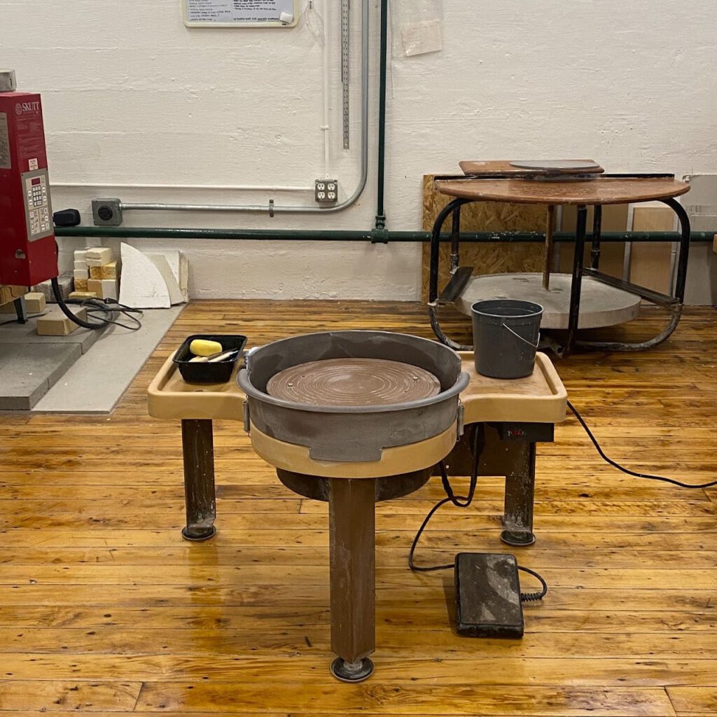 A pottery wheel in a studio with another work area in it